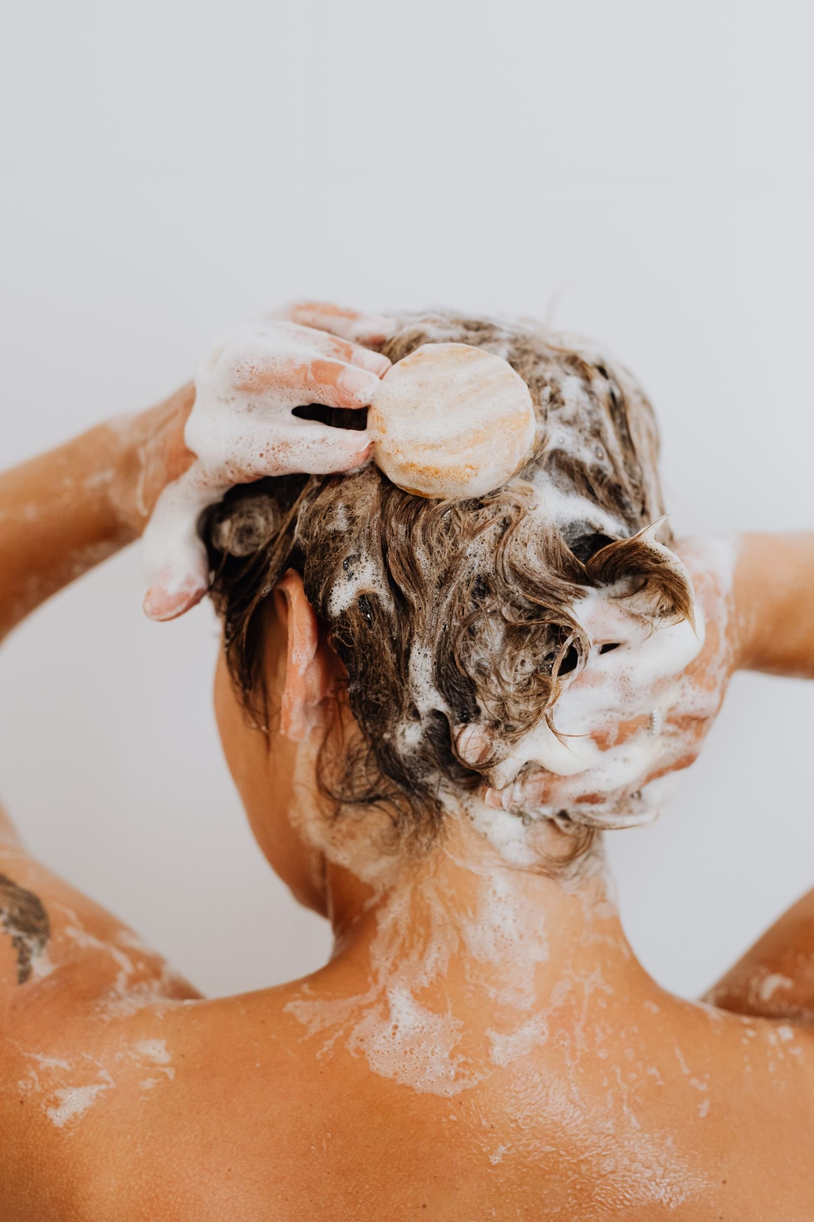 Woman washing her hair with shampoo, learning how to get rid of dandruff