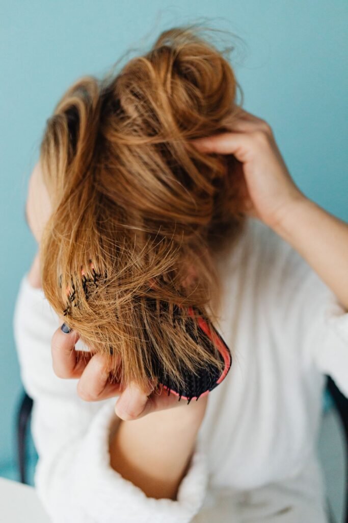 Woman gently brushing her hair, a daily habit that can cause or prevent breakage